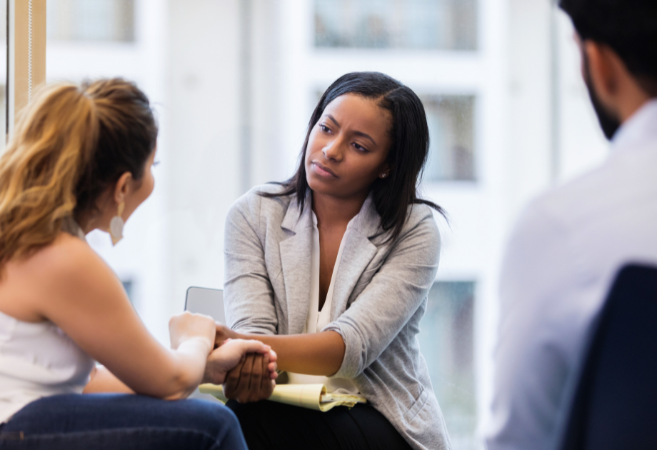 two women engaged in a conversation, holding hands. One of the women look uncomfortable